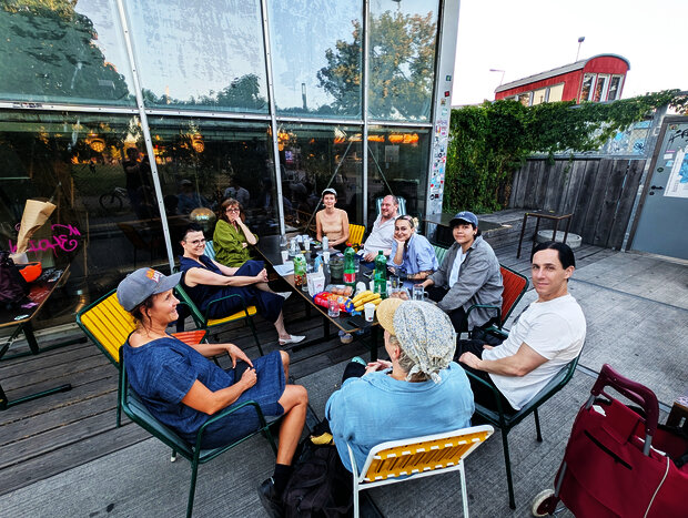 Foto: Susanne Rogenhofer 10 Personen sitzen rund um einen Tisch auf einer Terasse (des Flucc) und schauen großteils in RIchtung Kamera.