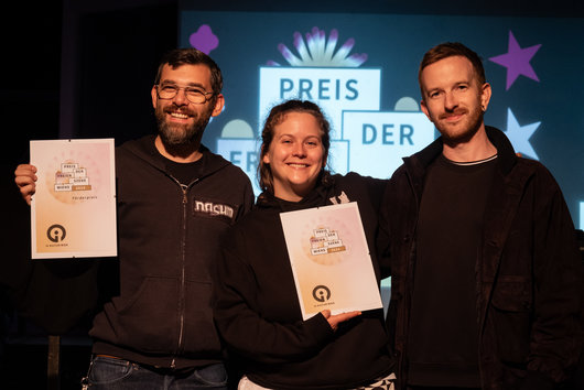 Die Gewinner*innen aus dem Venster99 und vom 4lthagrund mit Preisurkunden auf der Bühne (Link zu Text im Portal preis.igkulturwien.net)