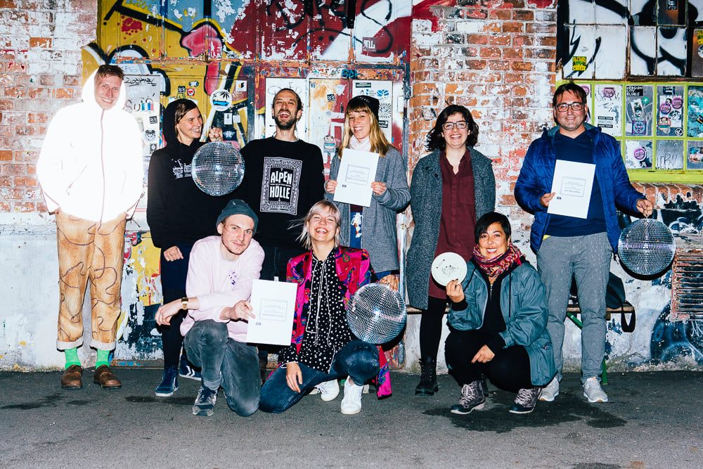 Gewinner*innen der Preise der freien Szene Wiens und der Sonderpreise für Clubkultur, vor einer Wand in der Arena posierend